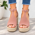 A pair of women's peep-toe platform wedge sandals in dusty rose pink faux suede with perforated detailing, featuring an ankle strap and braided jute espadrille-style soles, shown on a model's feet.