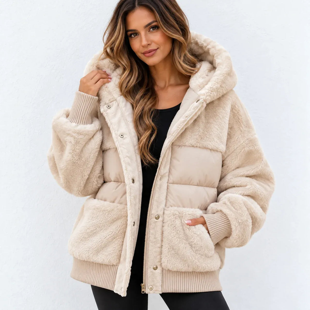 A woman wearing a beige sherpa-lined puffer jacket with a plush hood, ribbed cuffs, and front pockets, styled over a black top against a light gray background.