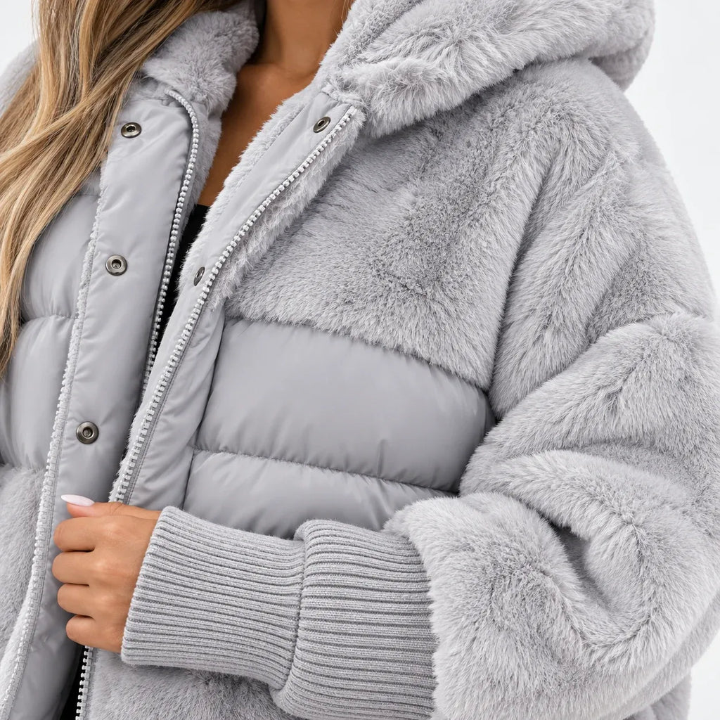 A close-up of a person wearing a light gray hooded puffer jacket with faux-fur trim and ribbed knit cuffs, shown against a plain light background.