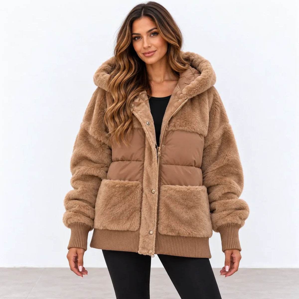 A woman modeling a tan faux fur puffer jacket with a matching faux fur hood, featuring a quilted front panel, ribbed cuffs, and front pockets, set against a plain white studio background.