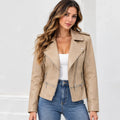 A woman wearing a beige faux-leather moto jacket with silver zippers, styled over a white tank top and blue jeans, set against a clean white background.