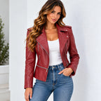 A woman wearing a burgundy faux leather moto jacket with silver zippers, styled over a white tank top and blue jeans, posing against a clean white wall.