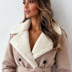 A woman wearing a beige trench coat with a thick cream sherpa lining, photographed against a plain light gray wall.