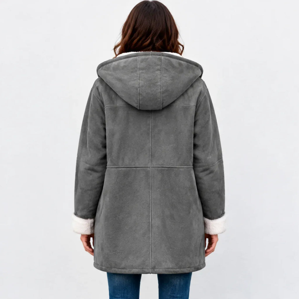 A woman viewed from the back wearing a gray hooded shearling-style coat with white faux-fur trim at the hood and cuffs, paired with blue jeans against a light gray studio background.