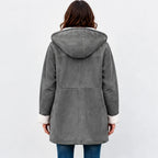 A woman viewed from the back wearing a gray hooded shearling-style coat with white faux-fur trim at the hood and cuffs, paired with blue jeans against a light gray studio background.