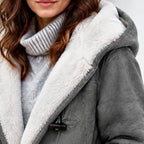 Close-up of a person wearing a gray suede-like hooded jacket with a thick white sherpa lining, paired with a light gray ribbed turtleneck sweater.