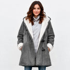 A woman wearing a gray suede-like hooded coat with a white sherpa lining, styled over a light gray turtleneck sweater and blue jeans, against a plain white studio background.