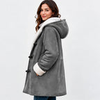 A woman wearing a gray hooded shearling-style coat with a white sherpa lining and toggle closures, photographed against a plain light gray studio background.