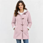 A woman wearing a light pink hooded duffle coat with white sherpa lining and brown toggle closures, paired with blue jeans, against a light gray studio background.