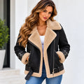 A woman wearing a black faux-leather shearling jacket with beige sherpa lining, paired with a white top and blue jeans, standing against a white wall.