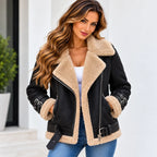 A woman wearing a black faux-leather shearling jacket with beige sherpa lining, paired with a white top and blue jeans, standing against a white wall.