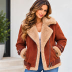 A woman wearing a brown suede aviator-style jacket with a beige sherpa lining, paired with a white top and blue jeans, standing in front of a light-colored wall.
