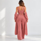 A woman stands with her back to the camera wearing a dusty rose two-piece outfit consisting of a cropped tank top and wide-leg pants, styled with a matching fuzzy open-front cardigan draped off her shoulders.
