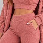 A close-up of a person wearing a fuzzy pink loungewear set, including a cropped long-sleeve top, matching high-waisted pants with side pockets, and a matching open cardigan.