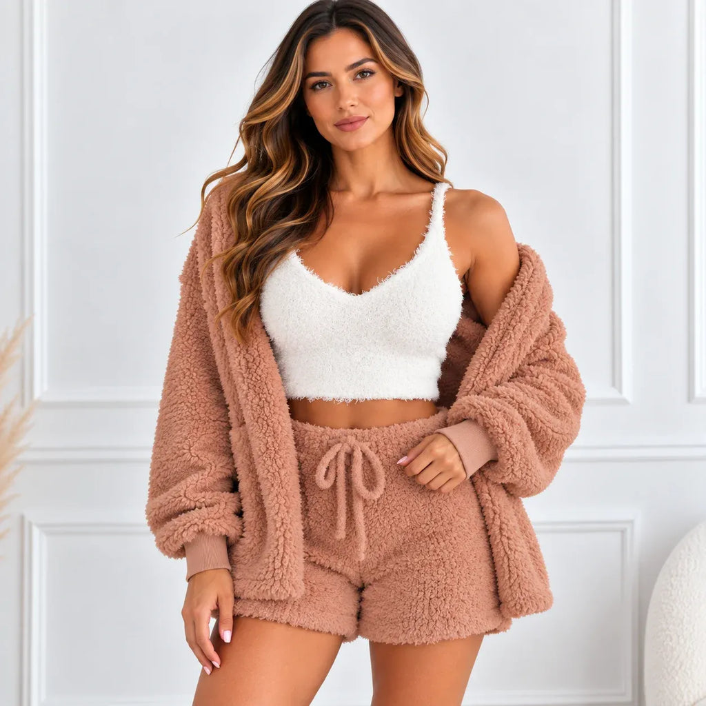 A woman models a cozy three-piece fleece loungewear set consisting of a matching cropped cardigan, bralette, and shorts in a dusty rose-brown color, paired with a white cropped camisole against a white paneled wall.