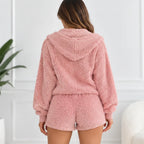 A woman viewed from behind wearing a pink sherpa fleece hooded sweatshirt and matching shorts in a bright indoor setting.