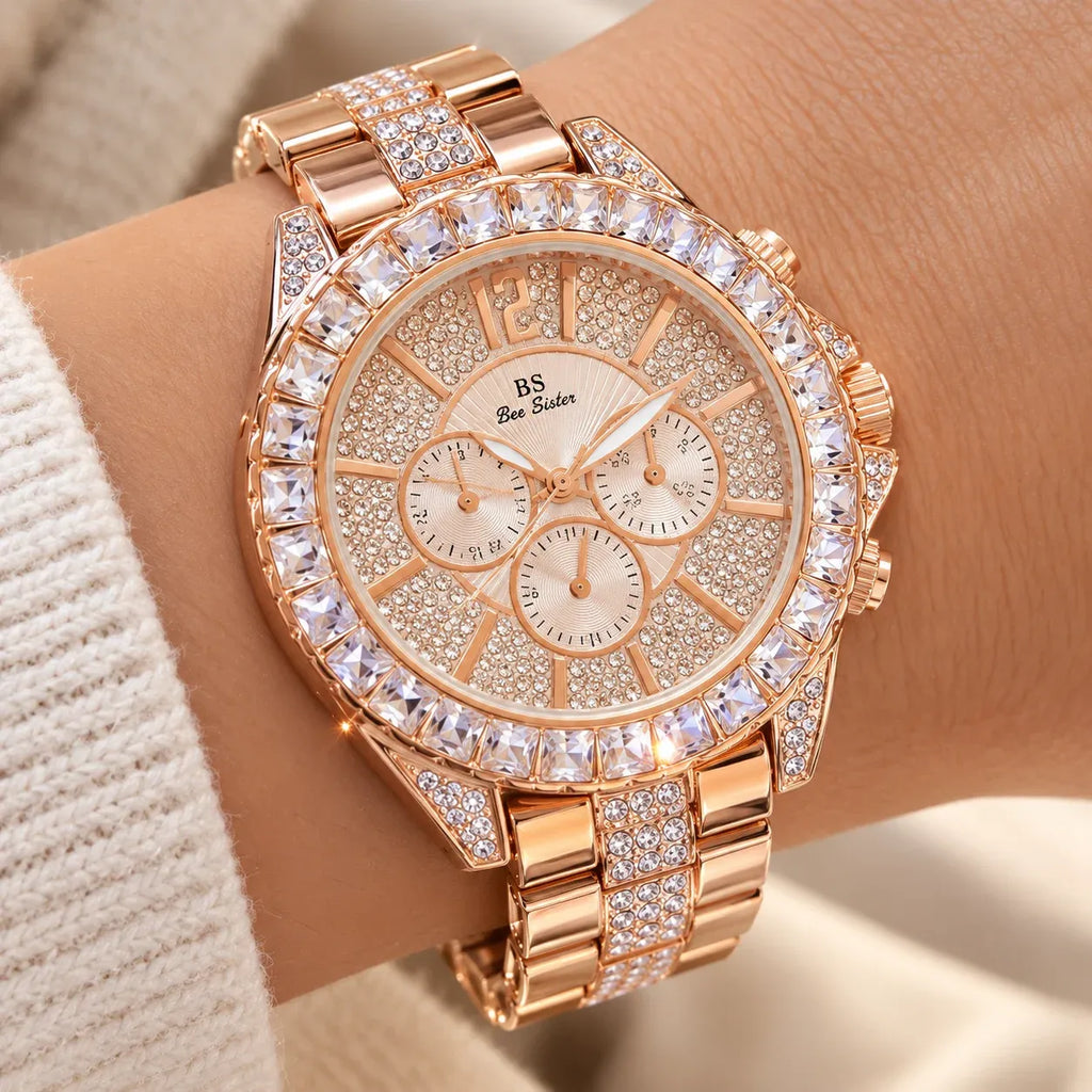 A close-up of a women's rose gold watch with crystal embellishments, worn on a wrist. The watch features a crystal-studded bezel, a matching crystal-link bracelet, and a beige dial with three sub-dials and the brand name 'BS See Diner'.