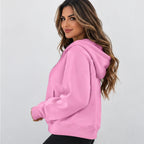 A woman wearing a pink pullover hoodie, photographed from the side against a plain light gray studio background.