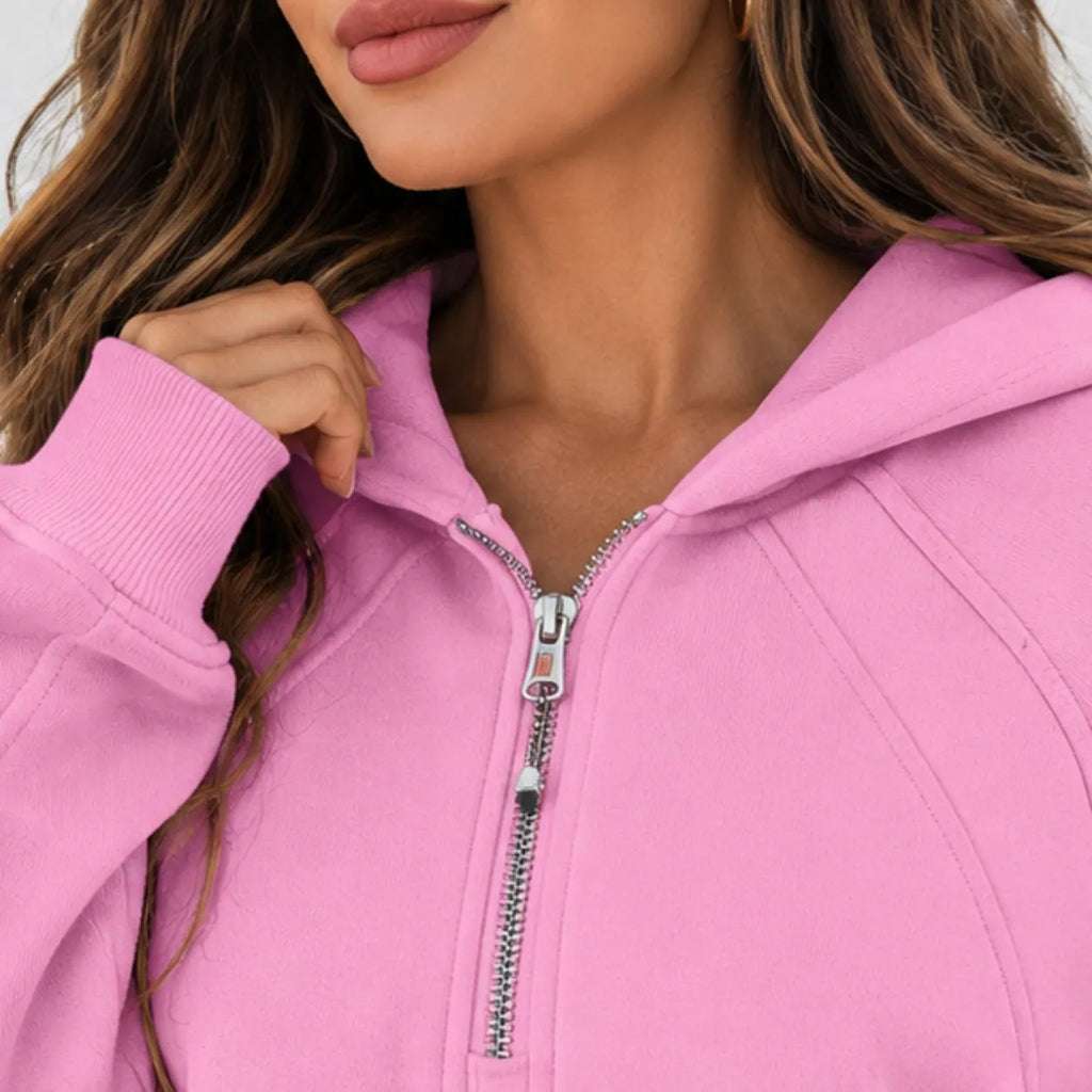 A close-up of a woman wearing a bright pink zip-up hoodie with a silver zipper and hood, cropped from the mouth down to the chest.