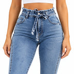 A close-up of a model wearing high-waisted light blue denim jeans with a ruffled paperbag waistband and a matching tie belt.