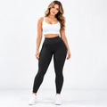 A woman modeling black textured high-waisted leggings with a white sports bra and white sneakers, standing against a clean white studio background.