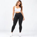 A woman modeling black textured high-waisted leggings with a white sports bra and white sneakers, standing against a clean white studio background.