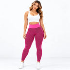 A woman modeling high-waisted athletic leggings with a pink and magenta geometric pattern, paired with a white sports bra and white sneakers, against a plain white studio background.