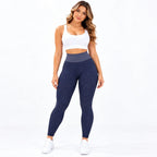 A woman modeling high-waisted navy blue textured leggings with a contrasting gray waistband, paired with a white sports bra and white sneakers, against a solid white background.