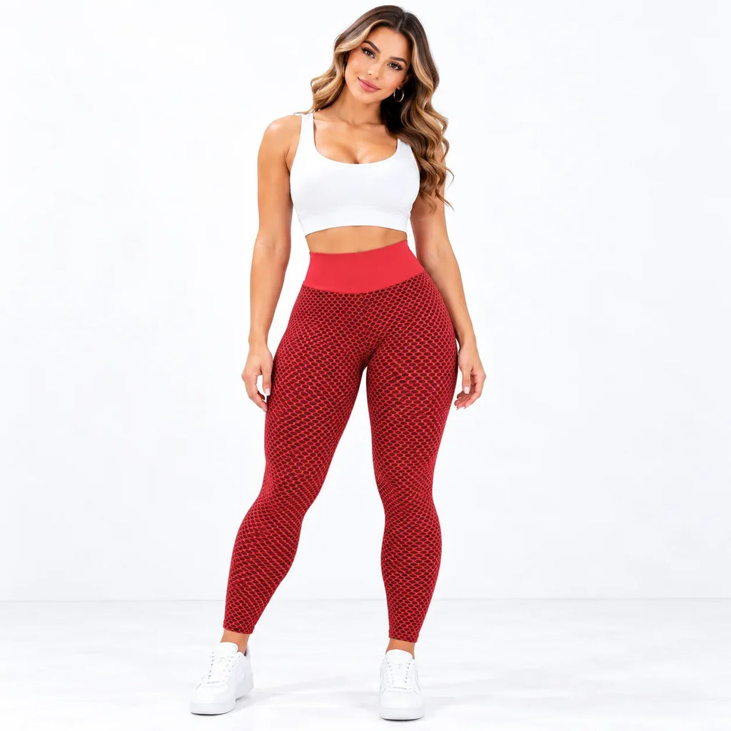 A woman modeling high-waisted red patterned leggings with a solid red waistband, paired with a white sports bra and white sneakers, against a plain white studio background.