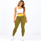 A woman modeling high-waisted athletic leggings with a yellow and black geometric pattern, paired with a white sports bra and white sneakers, against a plain white studio background.