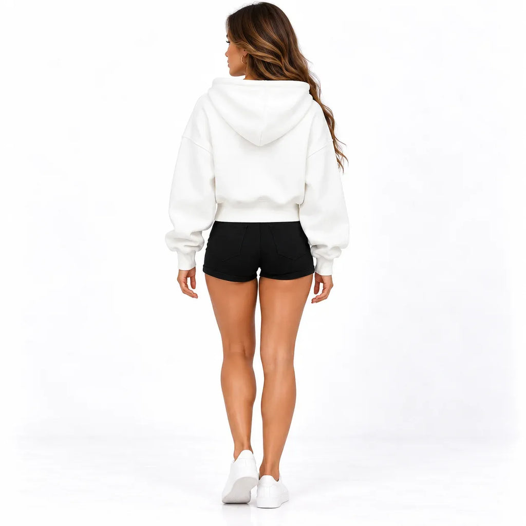 A woman shown from the back wearing a white cropped hoodie, black shorts, and white sneakers against a clean white studio background.