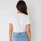 A woman viewed from behind wearing a plain white short-sleeve crop top and light blue jeans against a light gray background.