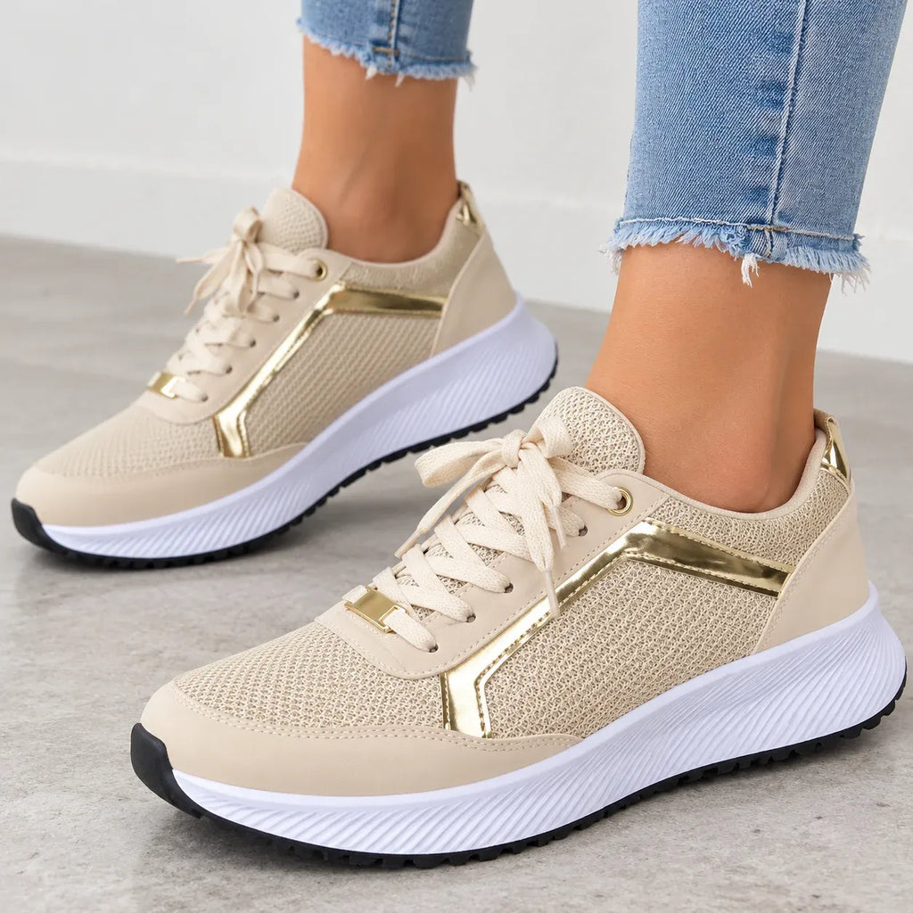 Beige mesh sneakers with metallic gold side accents, worn with light blue frayed-hem jeans on a gray floor.