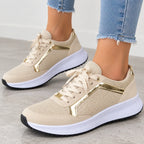 Beige mesh sneakers with metallic gold side accents, worn with light blue frayed-hem jeans on a gray floor.