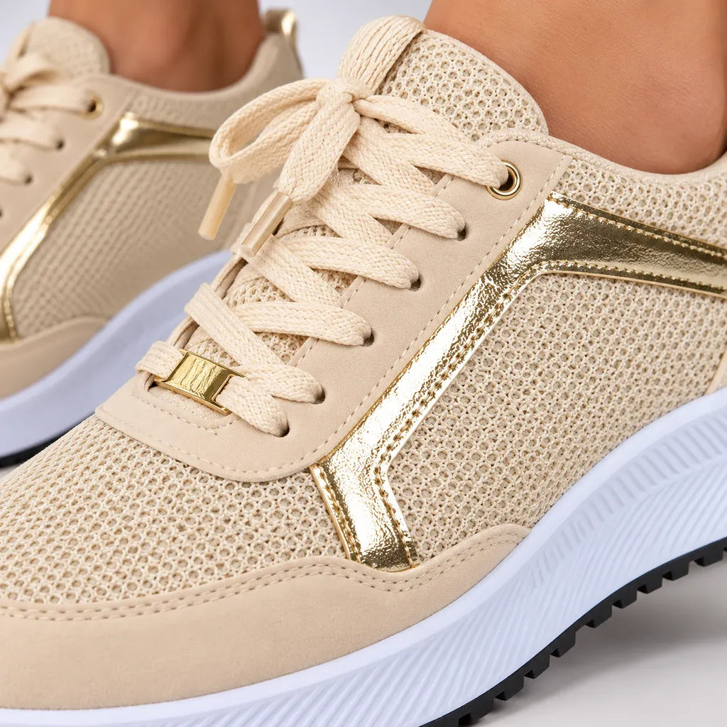 Beige mesh sneakers with metallic gold accents and white soles, shown on a model's feet.