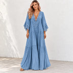 A woman modeling a light blue maxi dress with a lace V-neckline and tiered skirt, standing against a white wall.