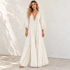 A woman models a bohemian-style maxi dress in a warm off-white/cream color. The dress features a deep V-neckline adorned with intricate lace applique, wide three-quarter length bell sleeves with lace cuffs, and a tiered, flowing skirt.