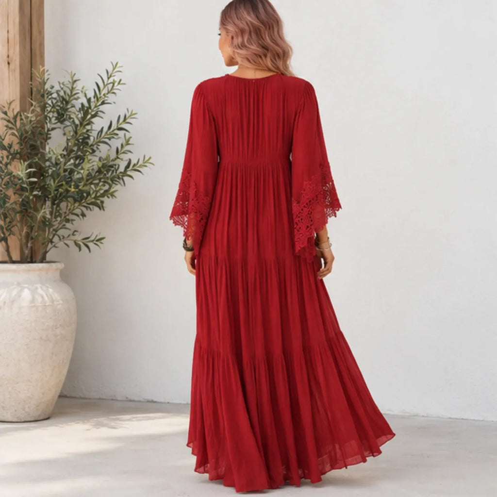 A woman wearing a long red maxi dress with three-quarter lace sleeves, shown from the back in a bright indoor setting with a white wall and a potted plant.