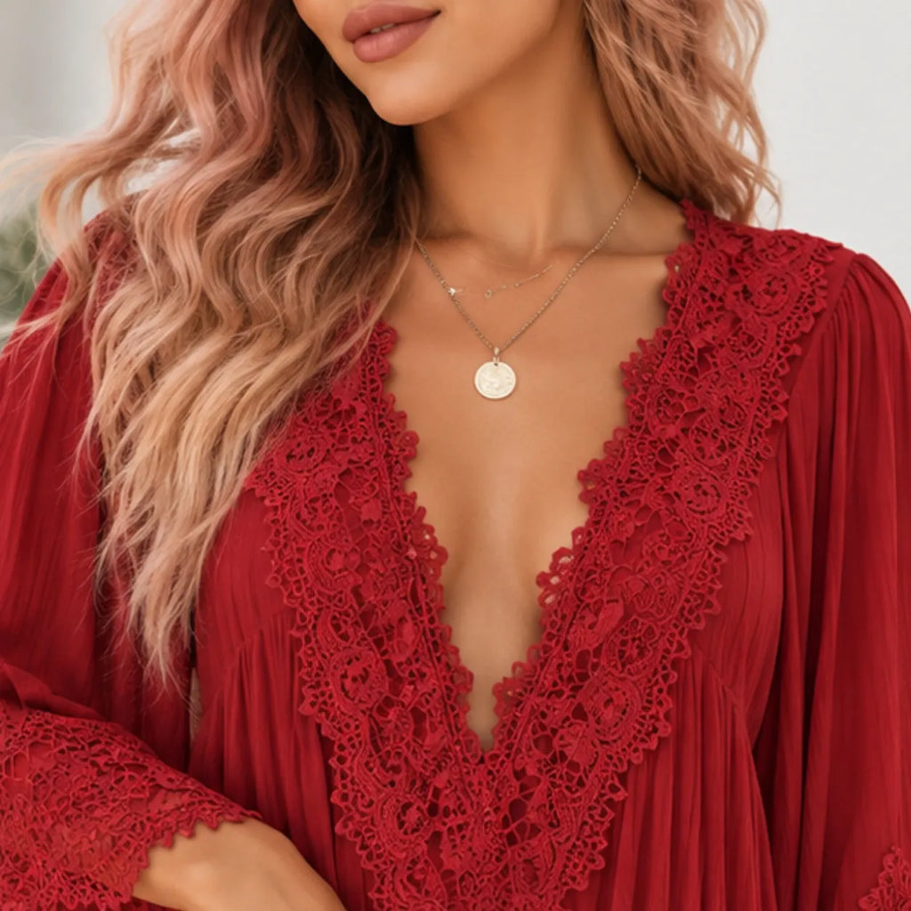 A close-up of a woman wearing a red long-sleeve blouse with a deep V-neck and intricate lace trim, styled with layered silver necklaces.