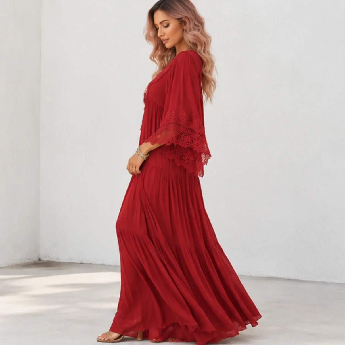 A woman modeling a long red maxi dress with flutter sleeves and lace trim, standing in a bright white room corner.