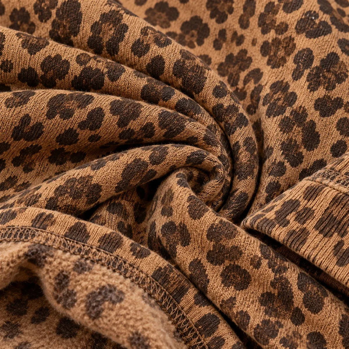 Close-up of a leopard-print knit fabric with a brown and tan base and dark brown spots, shown in soft folds with a ribbed edge.