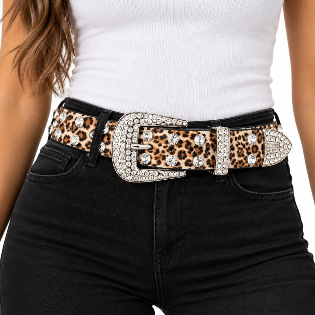 A close-up of a model wearing a leopard print belt with a large silver-tone buckle embellished with rhinestones, styled with a white ribbed top and black jeans.