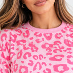 A close-up of a woman wearing a pink crewneck sweatshirt with a bright pink leopard print pattern.
