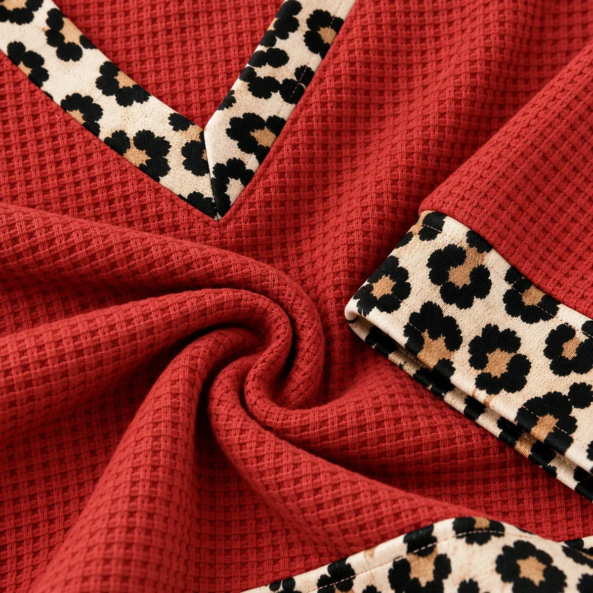 A close-up of a red waffle-knit fabric with beige leopard-print trim along curved edges, arranged in a spiral fold pattern.
