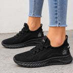A pair of black slip-on mesh sneakers worn with light blue frayed-hem jeans, shown from the side on a gray concrete floor.