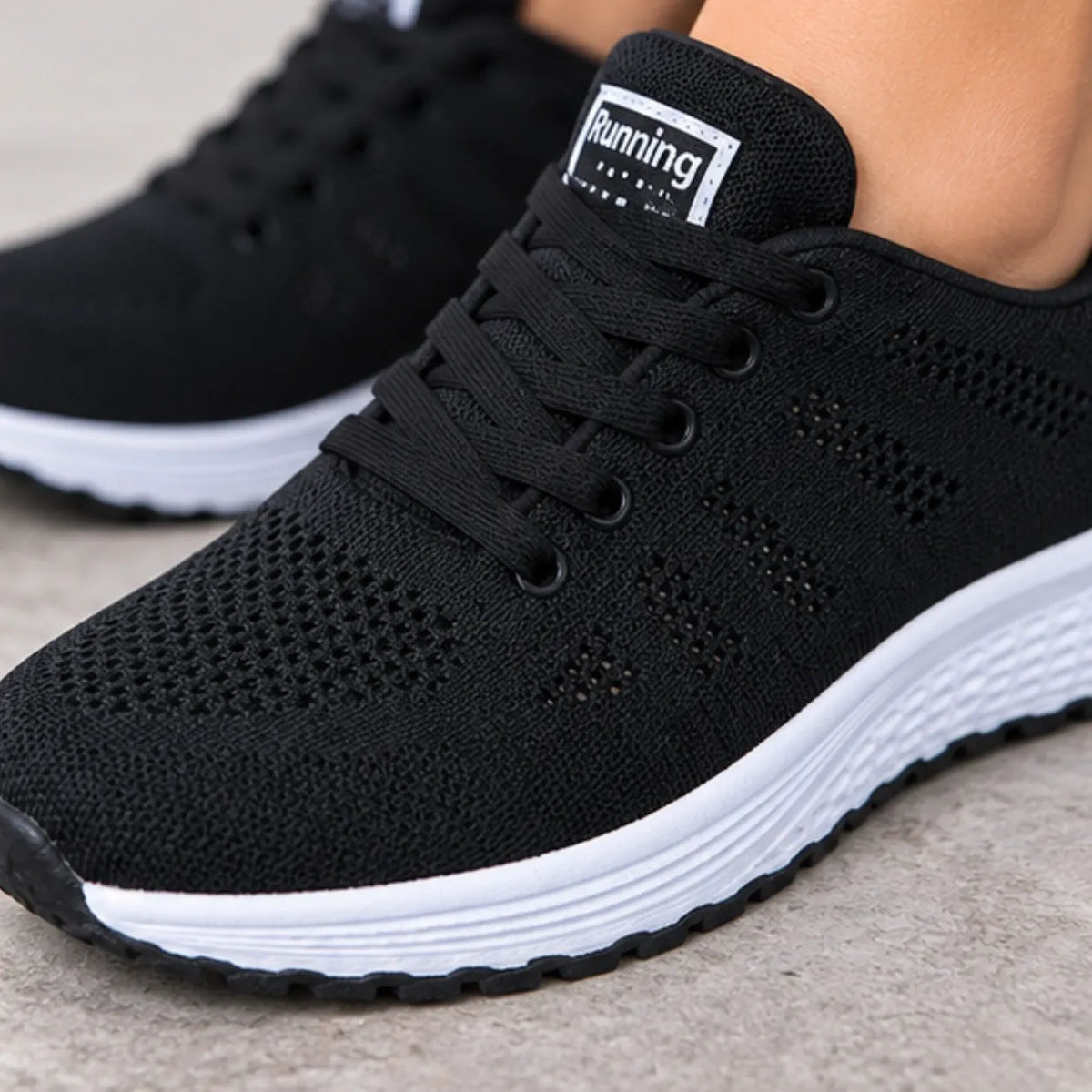 Black knit athletic sneakers with white soles, shown on a person's foot with the tongue label reading 'Running'.