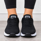 A pair of black athletic sneakers with white midsoles, shown on a person's feet wearing black leggings. The tongue of each shoe displays a white label with the brand name 'Running Machine'.