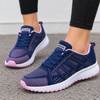 A pair of women's athletic sneakers in navy blue and pink, shown being worn with black leggings on a gray asphalt surface.