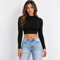A woman modeling a black long-sleeve mock neck crop top paired with light-wash distressed blue jeans against a plain white background.