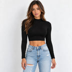 A woman modeling a black long-sleeve mock neck crop top paired with light-wash distressed blue jeans against a plain white background.